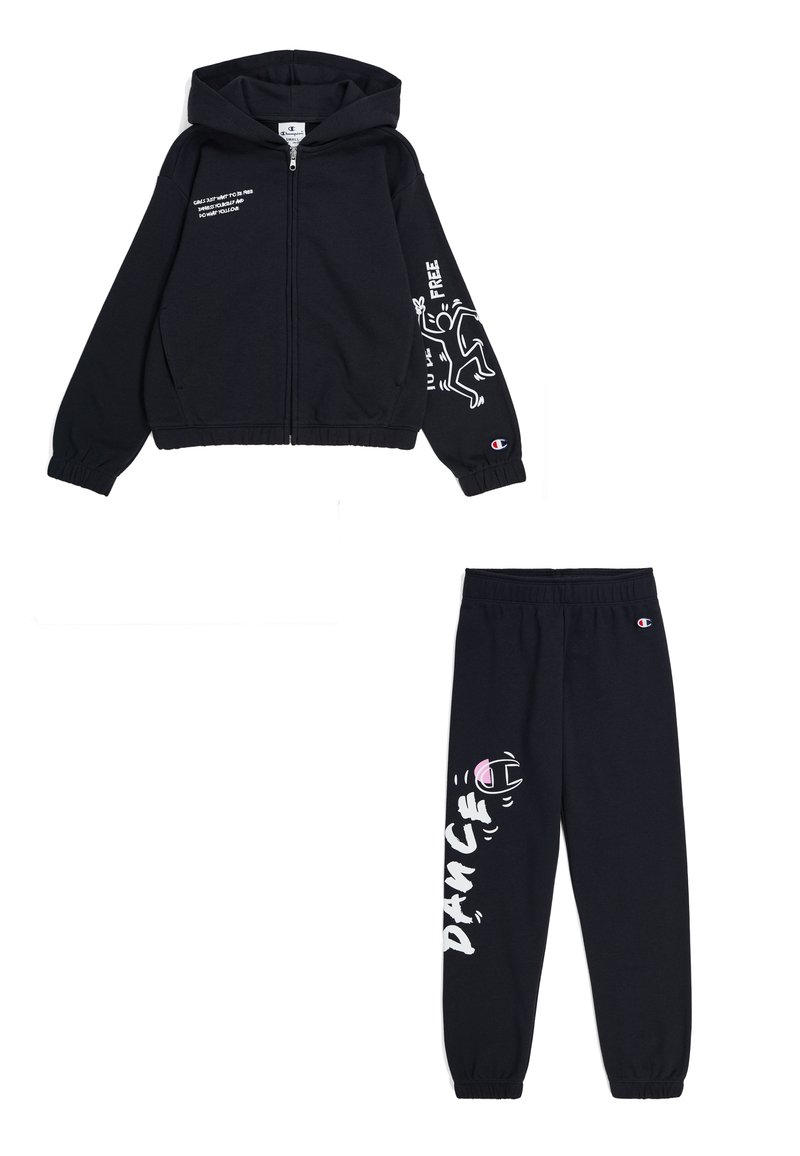Felpa nera con zip e cappuccio, caratterizzata da stampe grafiche sulle maniche. Pantaloni da tuta neri abbinati con la scritta "DANCE". Entrambi in un tessuto morbido.