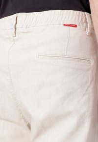 Világos bézs színű nadrág, puha anyagból, rugalmas derékgumival, hátul egy zsebbel és egy kis piros "JOOP! JEANS" címkével.