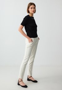Black short-sleeve top with a textured design, paired with white tailored pants and black flats featuring ankle straps. Simple and modern outfit.