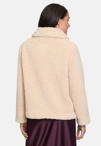 Kurtka z faux futra w miękkim beżu, z szerokim kołnierzem i długimi rękawami. Tkanina ma teksturowany, puszysty wygląd.