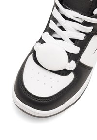 Pantofila alb-negru cu suprafață din piele, sistem de închidere cu șireturi albe rotunde, talpă texturată și vârf perforat pentru respirabilitate.