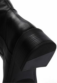 Bottine en cuir noir avec un talon empilé texturé, tige lisse et semelle en caoutchouc. Présente des coutures apparentes et un bout légèrement arrondi.