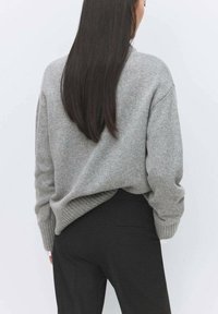 Suéter gris de punto con un ajuste relajado, puños acanalados y un diseño ligeramente holgado, combinado con pantalones negros de corte entallado.