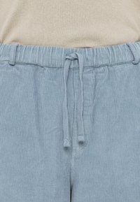 Helle blaue Cordhosen mit elastischem Bund und Kordelzug, die über eine senkrechte Rippstruktur verfügen und keine sichtbaren Hardwaredetails aufweisen.