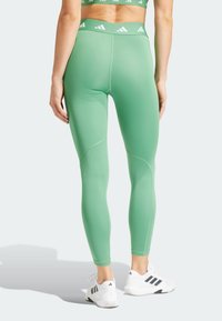 Gröna leggings med en slät yta, hög midja med logotyp och kontrasterande sömmar, tillsammans med vita träningsskor.