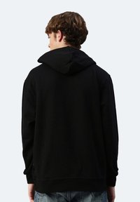 Felpa nera con cappuccio realizzata in tessuto morbido, caratterizzata da una vestibilità rilassata e polsini a costine. La parte posteriore ha un design semplice senza decorazioni.