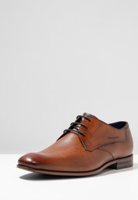 Chaussure habillée en cuir marron avec une finition texturée. Elle possède une pointe effilée, des lacets ronds et un petit talon avec de subtils rayures horizontales en accent.