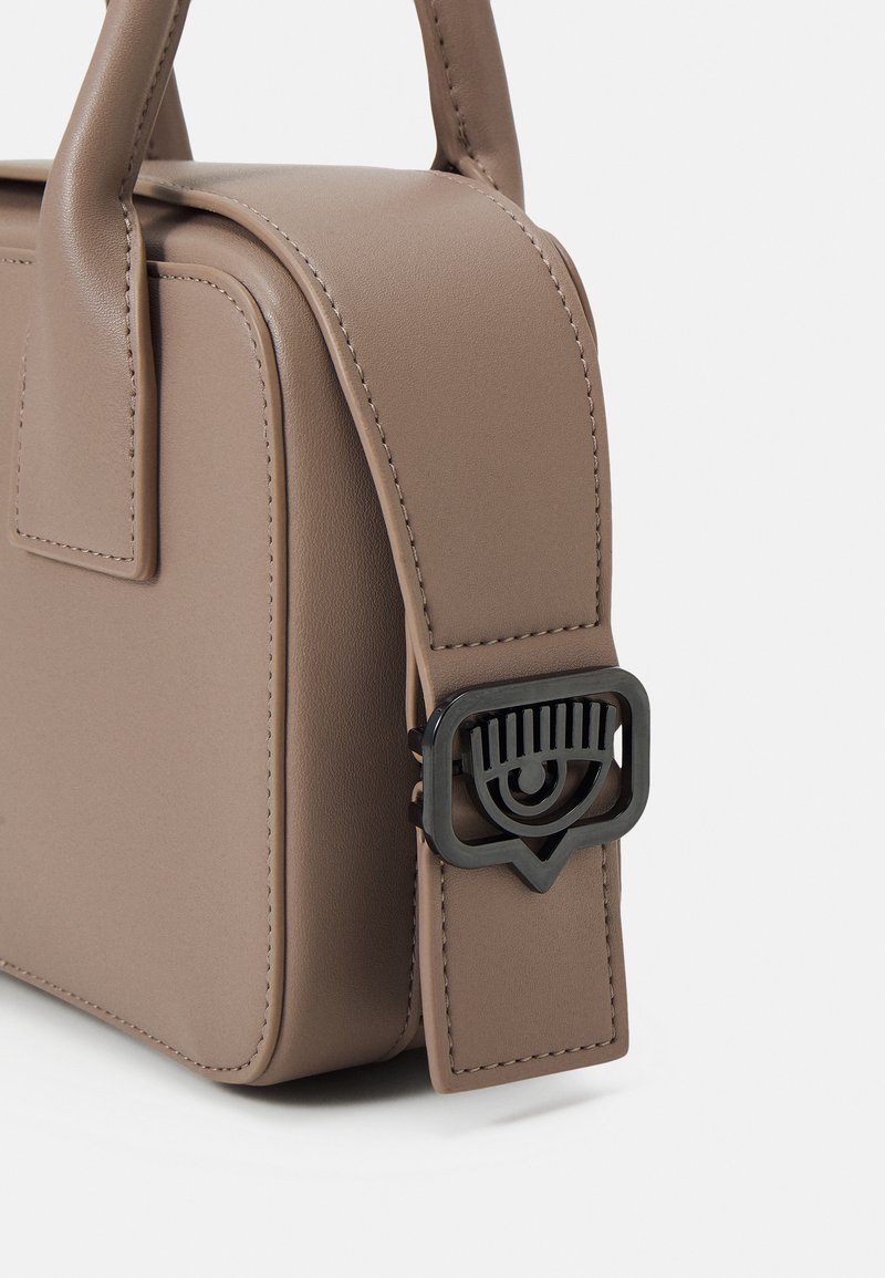 Torebka skórzana w kolorze taupe z haftowanymi brzegami i paskiem na ramię, z dekoracyjną klamrą w kształcie oka wykonaną z czarnego metalu.