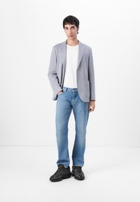 Blazer a quadri grigi sopra una t-shirt bianca, jeans blu e sneakers nere. Il blazer ha un rever a punta e due tasche frontali.