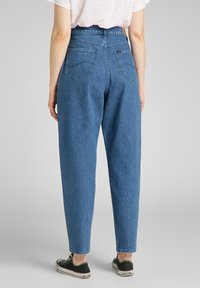 Jeans in denim blu a vita alta con una vestibilità rilassata, tasche posteriori e gamba leggermente affusolata. Abbinati a sneakers nere e bianche.