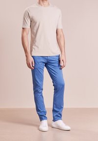 Beige bomulls-T-shirt i kombination med blå chinos, kompletterad med vita sneakers. Passformen är slim och tyget har en slät yta.