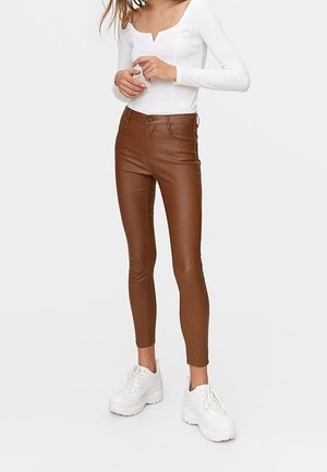Pantalones skinny de imitación de cuero marrón con una cintura alta, estilo de cinco bolsillos y sutiles detalles de costura, combinados con zapatillas blancas de plataforma.