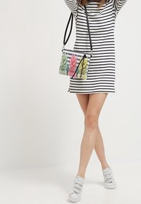 Torebka na ramię z przezroczystym wzorem, ozdobiona kolorowymi obrazkami ananasa na tle czarno-białych pasków. Wykonana z materiału syntetycznego.