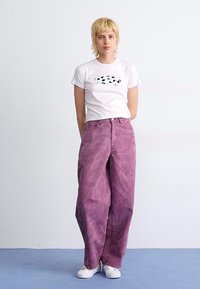 Purple, wide-leg jeans with a faded texture, paired with a white T-shirt featuring a black graphic design, worn with white sneakers.