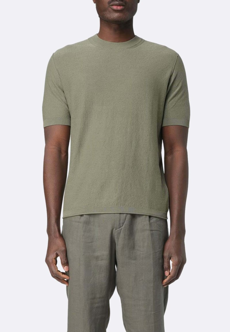 T-shirt verde oliva a maniche corte con collo rotondo a costine, realizzato in un tessuto strutturato, abbinato a pantaloni in lino grigio chiaro.