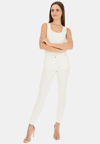 Biała bezrękawnik z okrągłym dekoltem, zestawiony z białymi obcisłymi dżinsami i beżowymi sandałami na obcasie, prezentujący dopasowany krój.