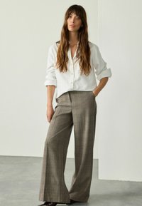 White button-up shirt with rolled sleeves, paired with wide-legged, brown plaid trousers. Smooth texture, relaxed fit, and tailored design.