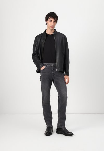 Blouson en cuir noir, t-shirt noir, jean slim gris, et bottines noires. Textures lisses et accents matériels minimalistes visibles.