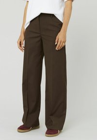 Pantalons marron à rayures avec une coupe large, fabriqués dans un tissu lisse, dotés de poches avant et d'une coupe ajustée.