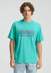 Turquoise katoenen T-shirt met korte mouwen en een golvend grafisch patroon in blauw en wit. Ronde hals, ontspannen pasvorm.