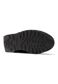 Suela de zapato deportivo negra con un patrón de banda de rodadura robusto, que presenta lugs prominentes y detalles de tracción circulares para mayor agarre. Bordes suaves.