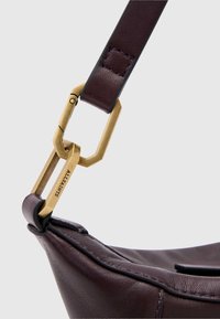 Bruine leren handtasriem met een messing sluiting met geometrische vormen, een gladde textuur en subtiele stikdetails.