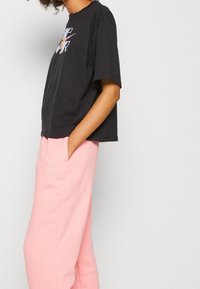 Svart bomullst-shirt med korta ärmar och färggrafisk design, tillsammans med avslappnade rosa sweatpants med en liten vit logotyp.