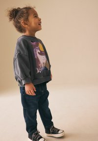 Sudadera gris con un gráfico de unicornio en púrpura y amarillo, combinada con vaqueros azul oscuro y zapatillas altas negras con suelas blancas.