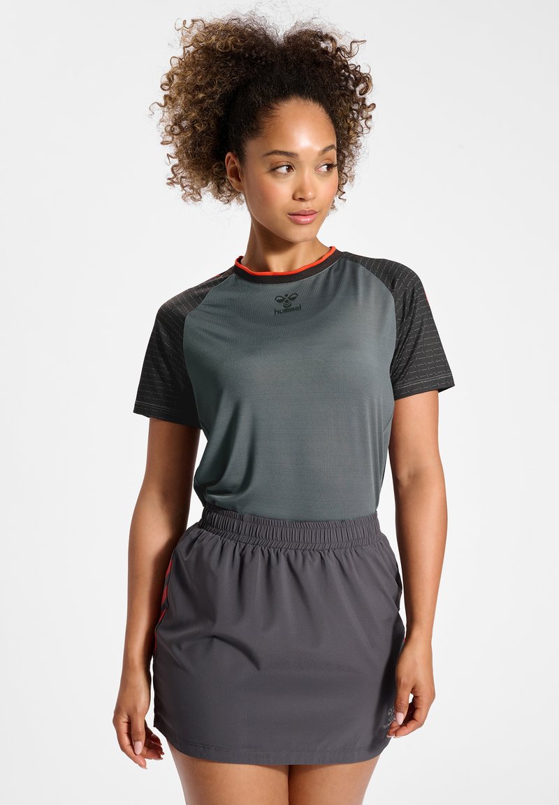 Grå sportstopp med texturerade svarta ärmar och röda detaljer, kombinerad med en grå kjol med elastisk midjeband. Lätta, andningsbara material.