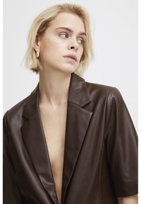 Blazer en cuir marron avec un décolleté en V profond, des manches courtes et un col structuré. Texture lisse avec une finition soignée.