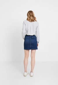 Mini falda de mezclilla en azul oscuro, con un corte recto, dos bolsillos traseros y un dobladillo limpio. Combinada con una camisa de botones de color gris claro.