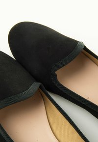 Scarpe slip-on nere in suede con bordi elastici, punta arrotondata e una soletta tan a contrasto. Texture liscia con dettagli minimi.