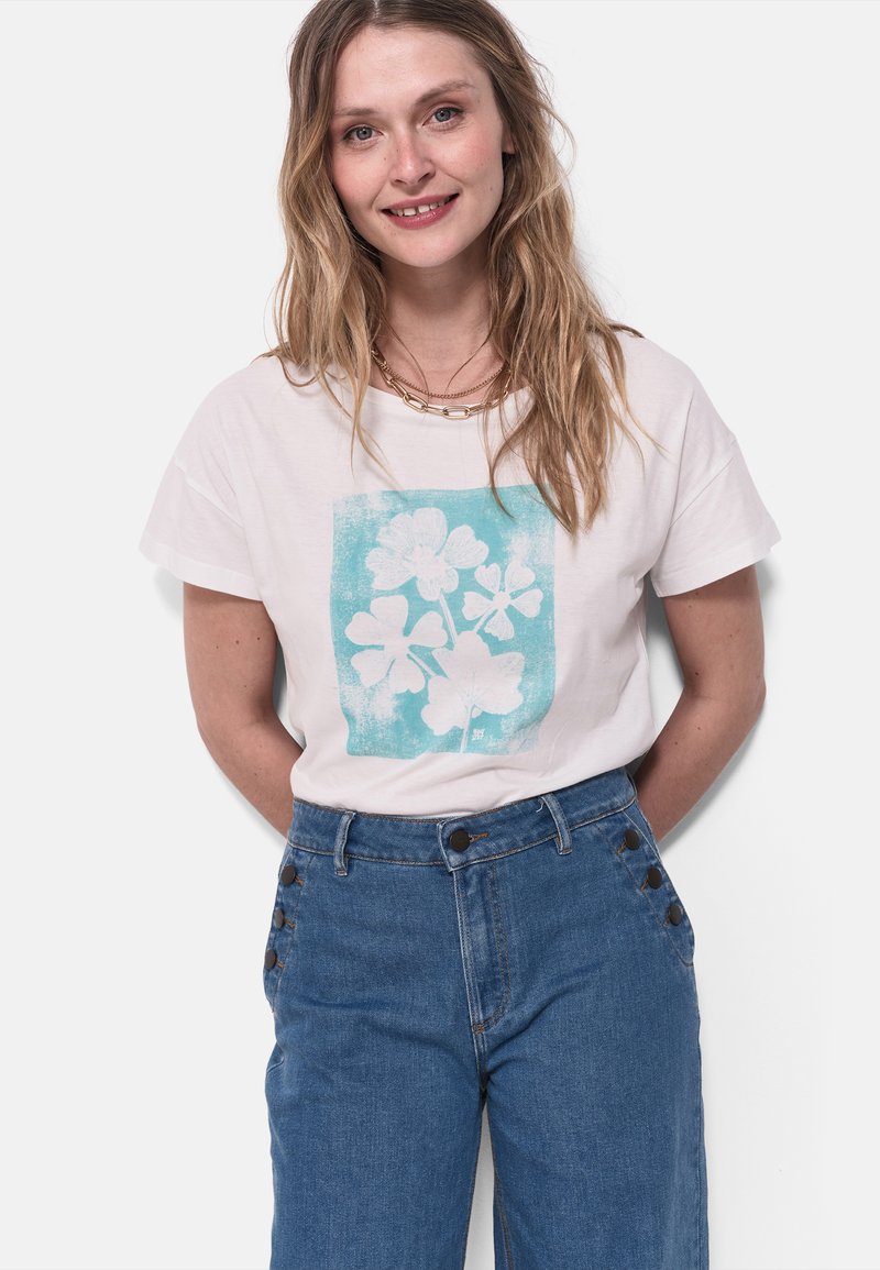 Camiseta de algodón blanca con un estampado floral turquesa, con un corte holgado y mangas cortas, combinada con pantalones de mezclilla azul de talle alto.
