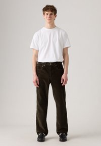 Tricou alb cu mânecă scurtă purtat împreună cu pantaloni de catifea întunecată, având un design cu picior dreaptă și detalii vizibile ale cusăturii buzunarelor.