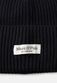 Gorro preto de malha com textura canelada. Apresenta um rótulo branco com o texto "Marc O’Polo" e "EST. IN STOCKHOLM".