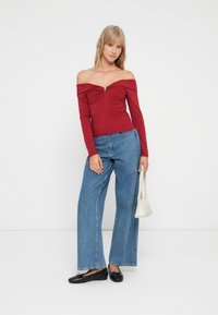 Top rojo sin mangas con fruncidos y un acento dorado central, combinado con unos vaqueros anchos de tiro alto en azul y planas negras. Incluye un bolso blanco.