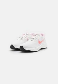 Zapatillas blancas con acentos rosas, hechas de material de malla. Presentan cordones, punta redondeada y una suela de goma negra texturizada.