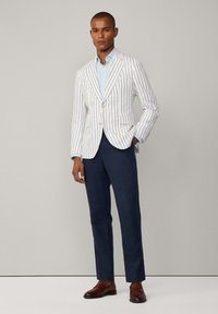 Blazer rayé blanc avec des lignes bleues, associé à une chemise bleu clair, un pantalon bleu marine foncé et des chaussures en cuir marron.