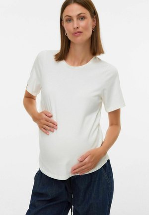 Femme avec des cheveux lisses de longueur épaules portant un t-shirt blanc et un pantalon sombre, tenant doucement son ventre de femme enceinte avec les deux mains.