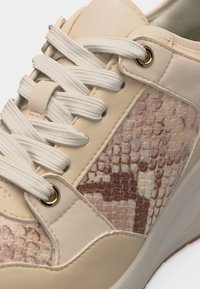 Baskets couleur crème avec lacets blancs et côtés texturés à imprimé serpent marron et beige, montrant les coutures et les œillets métalliques.