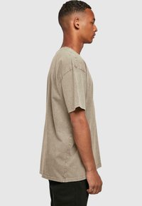 Kortærmet T-shirt med rund hals i lys khaki, med en støvet tekstur og synlige sting. Båret med sorte bukser.