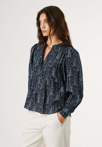 Jūrinė bluzonė su gėlių ir vertikalių juostų raštu, laisvas kirpimas, raukšlių detalė, aukštas apykaklė ir ilgos pūkuotos rankovės. Derinama su šviesiomis kelnėmis.