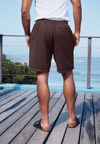 Czarne szorty z teksturą waflową, z elastycznym paskiem w talii i tylną kieszenią, zestawione z czarnymi sandałami na korkowej podeszwie.