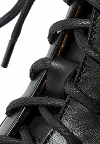 Detalle de zapatilla negra de cuero con cordones negros, superficie texturizada y diseño elegante. Los ojales destacan los elementos funcionales del zapato.