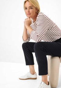 Haut rayé à manches longues en blanc et bordeaux, pantalon noir court et baskets blanches avec une semelle beige. Texture lisse, design décontracté.