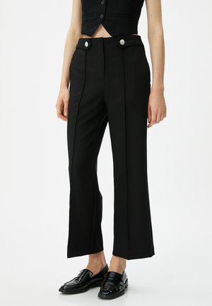 Pantalon noir ajusté en tissu lisse, doté d'une taille haute, de plis sur les côtés et de boutons argentés à l'avant.