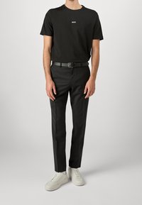 Černé tričko s logem "BOSS", doplněné o černé kalhoty na míru a bílé tenisky. Opasek je černý a střih je moderní a elegantní.