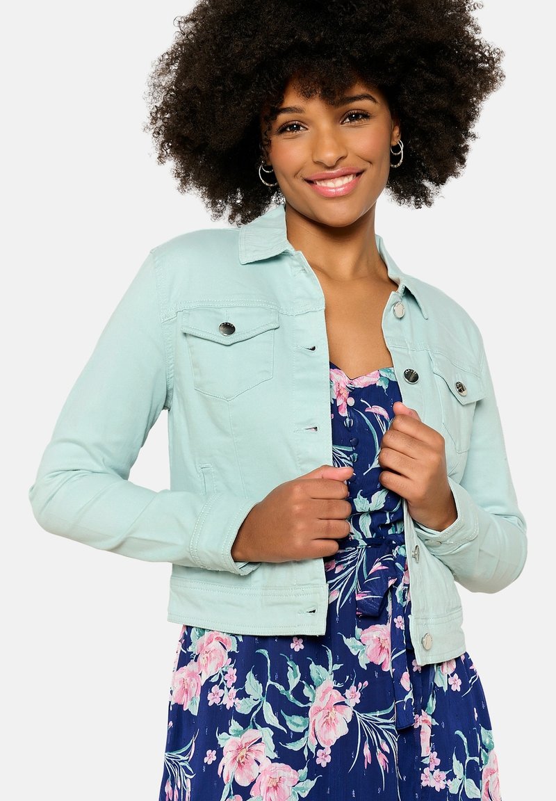 Müntz roheline denimpalt, millel on nup closure, eesmine taskud ja peen viik, kantud lillemustriga kleidi peal. Pehme tekstuur.