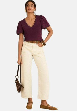 Haut bordeaux à bord scallopé avec des manches bouffantes, associé à un pantalon à jambes larges crème et des ballerines marron. Accessoirisé avec une ceinture et un sac.