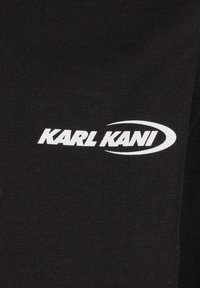 Black fabric t-shirt featuring a white "KARL KANI" logo. The fabric is smooth with a ribbed texture, showcasing a simple, clean design.